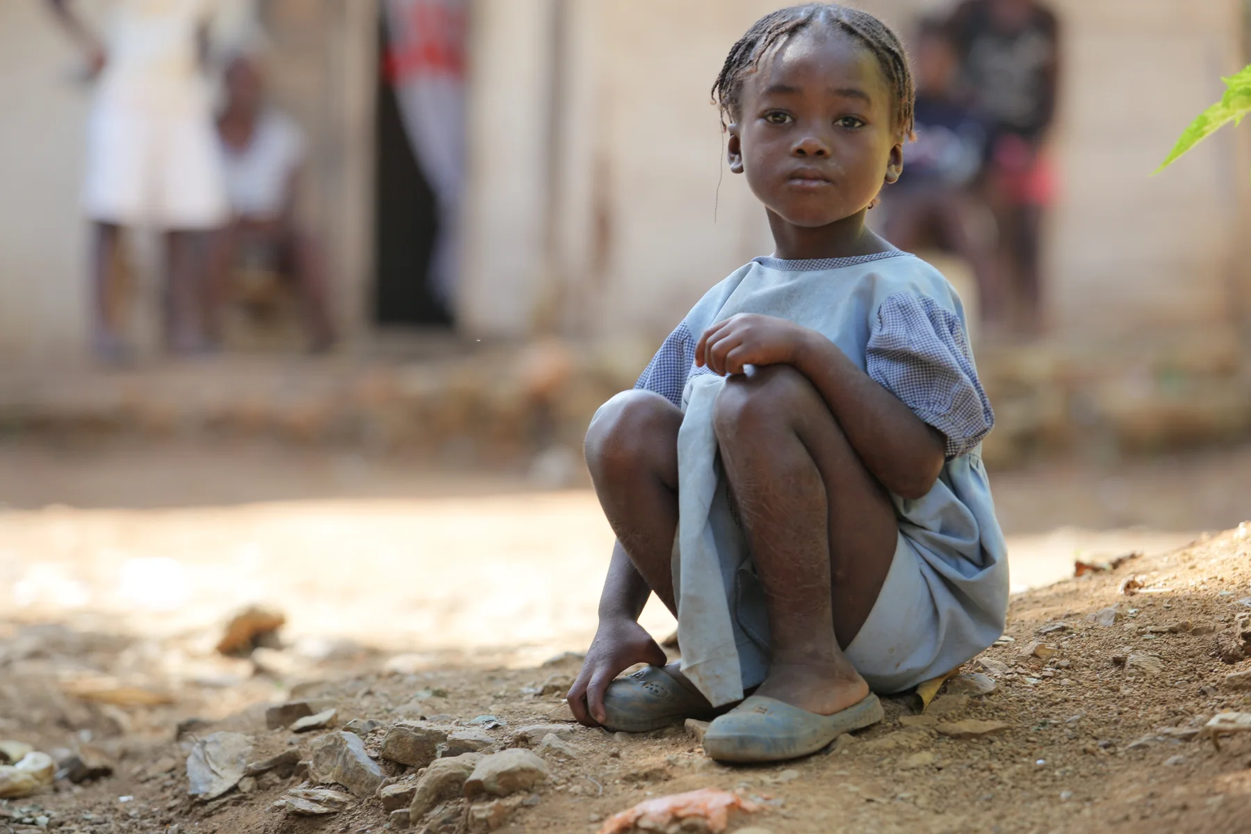 Menina sentada em frente a uma casa, no Haiti